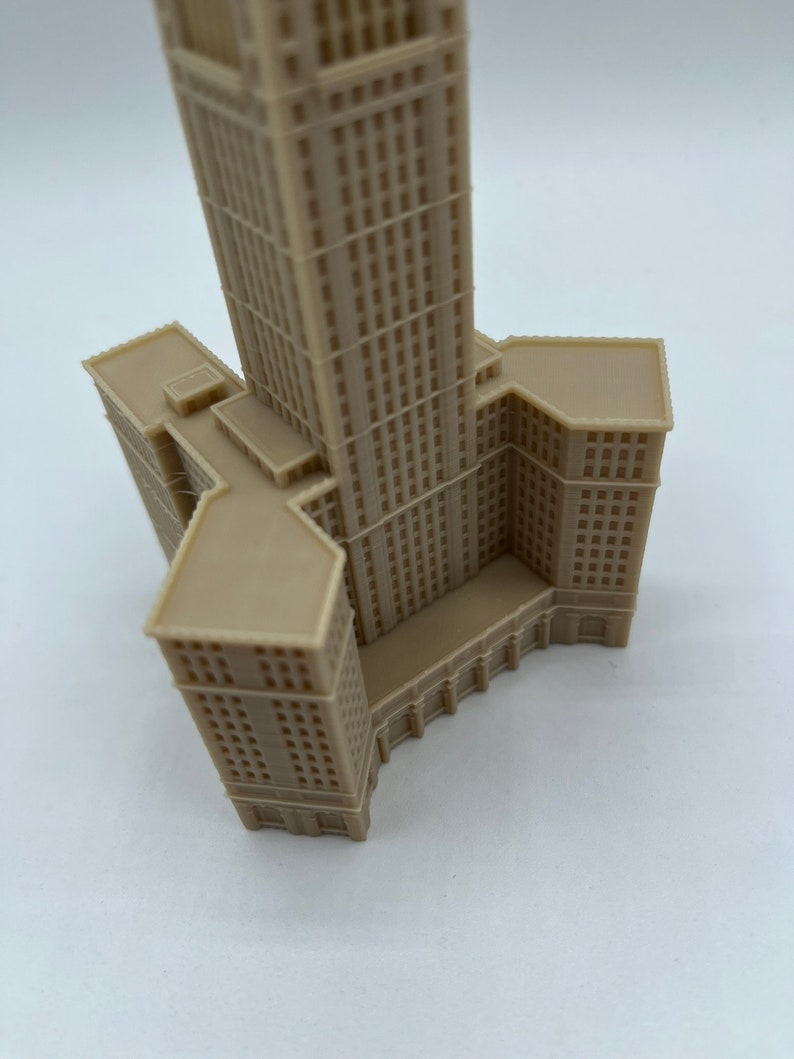 May include: A beige 3D printed model of a tall building with a square base and a pointed roof.