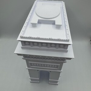 Może przedstawiać: Biały model architektoniczny Łuku Triumfalnego. Model przedstawia kultowy łuk, szczeg&oacute;łowe rzeźby i płaski dach z okrągłym wzorem. Model jest solidną, tr&oacute;jwymiarową reprezentacją.