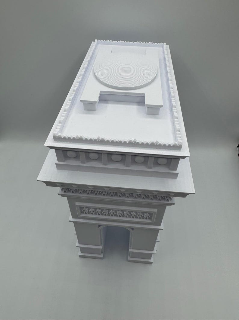 Może przedstawiać: Biały model architektoniczny Łuku Triumfalnego. Model przedstawia kultowy łuk, szczeg&oacute;łowe rzeźby i płaski dach z okrągłym wzorem. Model jest solidną, tr&oacute;jwymiarową reprezentacją.