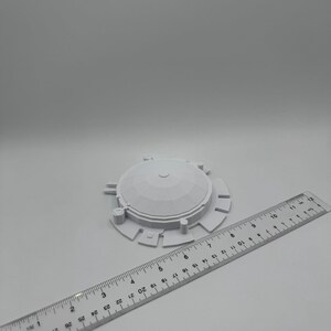 May include: A white, 3D-printed object with a domed top and circular base, next to a ruler. The object has a diameter of approximately 3 inches. The ruler is marked with inch measurements.