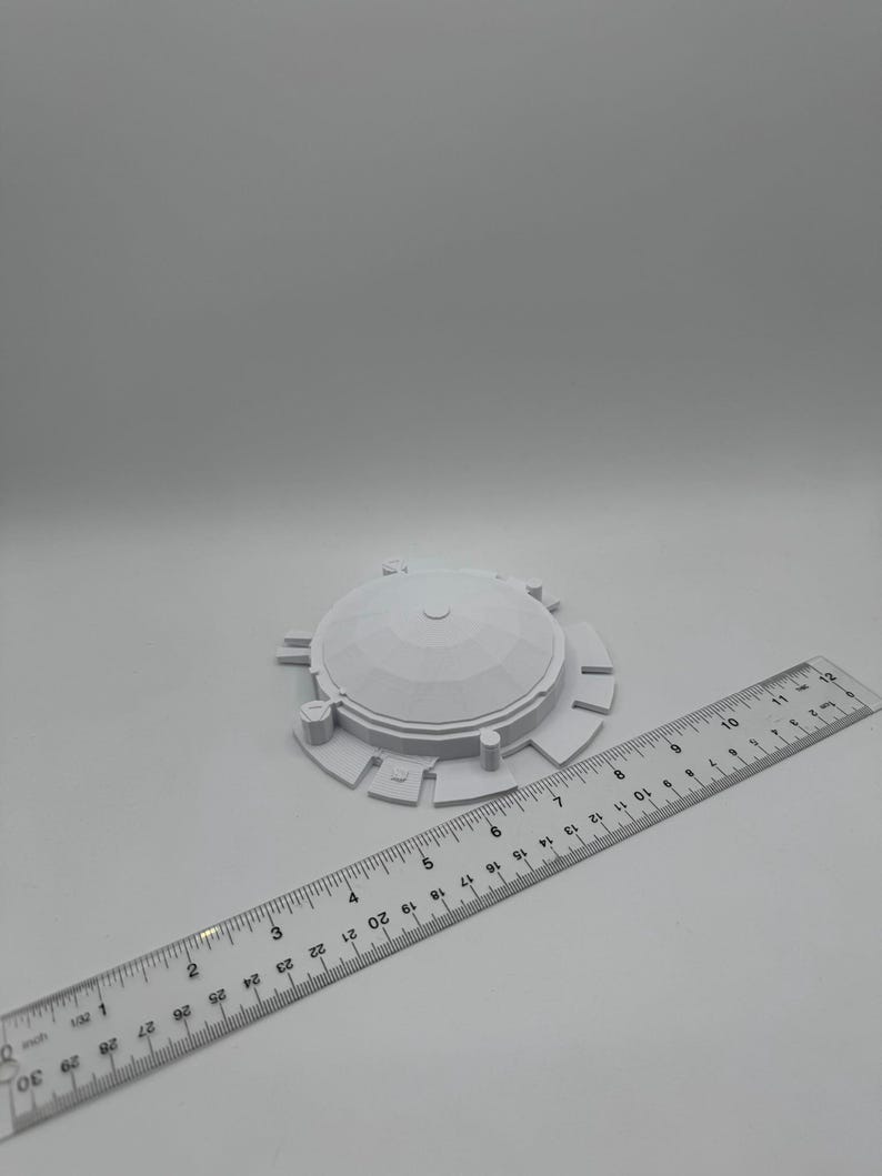 May include: A white, 3D-printed object with a domed top and circular base, next to a ruler. The object has a diameter of approximately 3 inches. The ruler is marked with inch measurements.