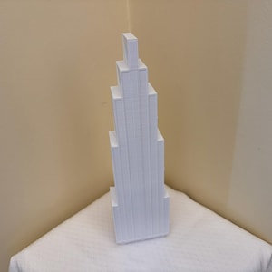 Puede incluir: Una torre alta y estrecha hecha de bloques rectangulares blancos apilados. La torre está hecha de un material blanco liso y tiene un diseño moderno y minimalista.