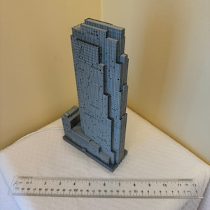 May include: A gray 3D printed model of a skyscraper building. The model is approximately 7 inches tall and has a detailed facade.