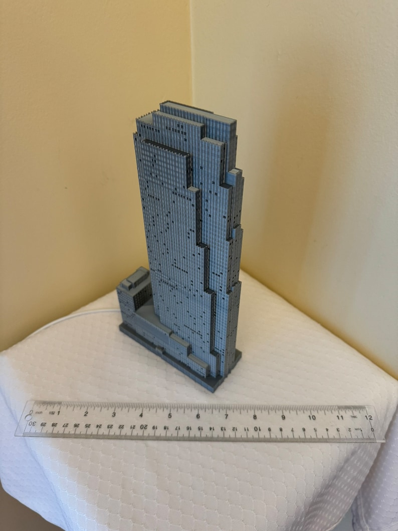 May include: A gray 3D printed model of a skyscraper building. The model is approximately 7 inches tall and has a detailed facade.