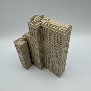 May include: A beige architectural model of a multi-story building with a smaller adjacent structure. The building has numerous windows and detailed architectural features, showcasing a classic design. The model is set against a plain background.