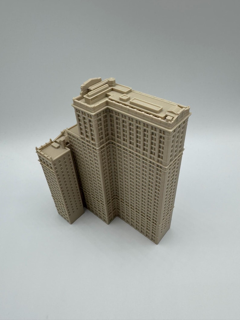 May include: A beige architectural model of a multi-story building with a smaller adjacent structure. The building has numerous windows and detailed architectural features, showcasing a classic design. The model is set against a plain background.