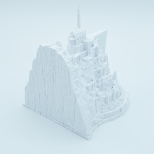 May include: A white 3D printed model of a castle on a cliff. The castle has a tall spire and many towers. The cliff is textured to look like rock.