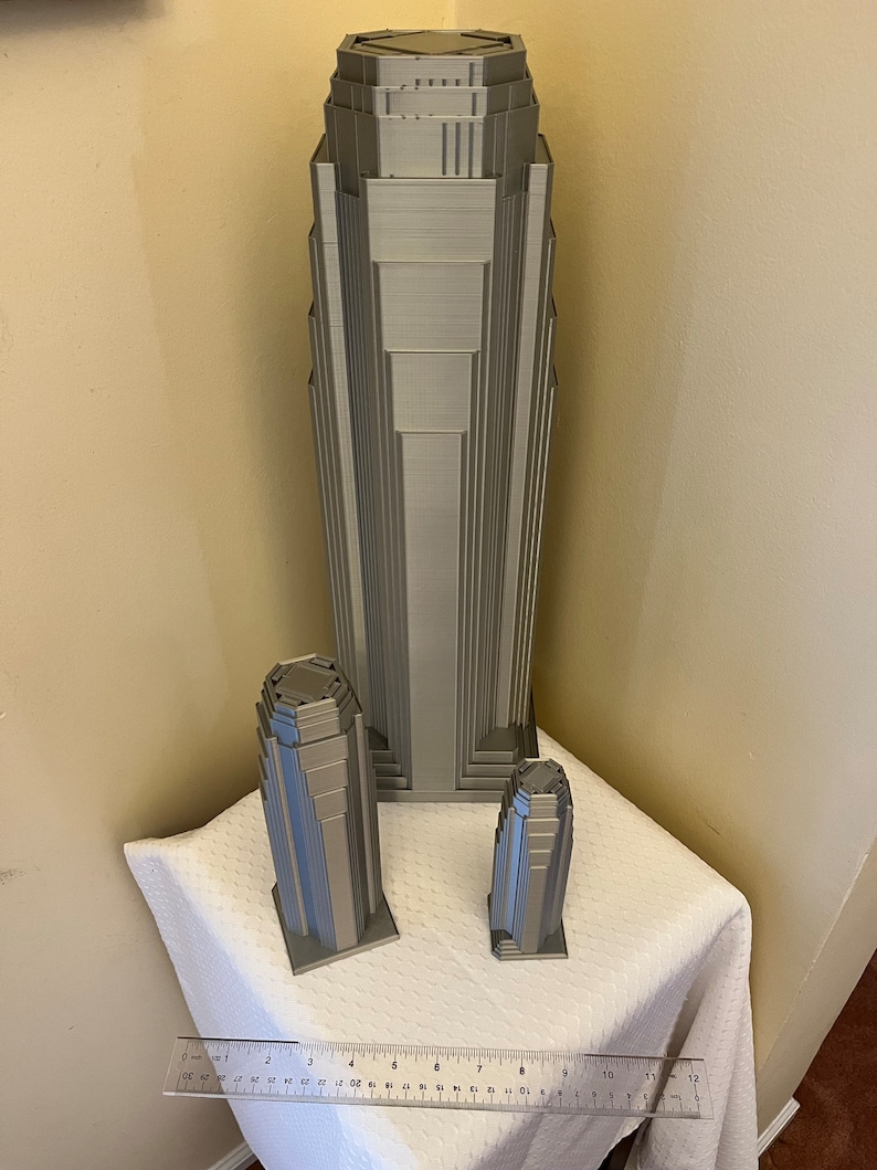 May include: Three 3D printed models of skyscrapers in a silver gray color. The tallest building is about 12 inches tall, the middle building is about 6 inches tall, and the smallest building is about 4 inches tall.