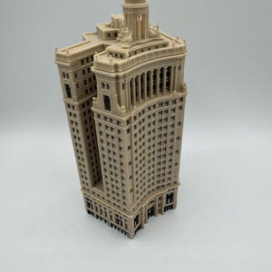 Op de afbeelding: Een gedetailleerd 3D-geprint model van een hoog, beige gebouw met een gebogen gevel en een koepelvormig dak.