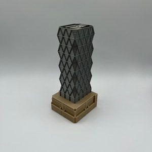 May include: A grey and black model of a skyscraper with a geometric design. The building has a brown base.