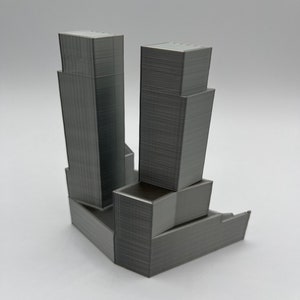 Op de afbeelding: Een 3D-geprint model van een grijs wolkenkrabbergebouw met een kleiner gebouw aan de zijkant.