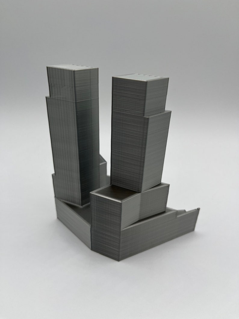 Op de afbeelding: Een 3D-geprint model van een grijs wolkenkrabbergebouw met een kleiner gebouw aan de zijkant.