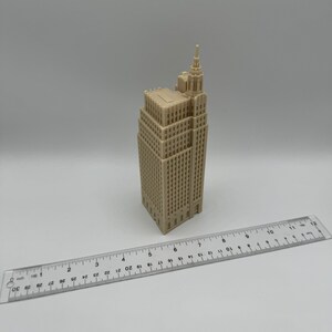Pu&ograve; includere: Un modello in miniatura beige di un edificio alto con un tetto a punta e molte finestre. Il modello &egrave; alto circa 15 cm e si trova su una superficie bianca.