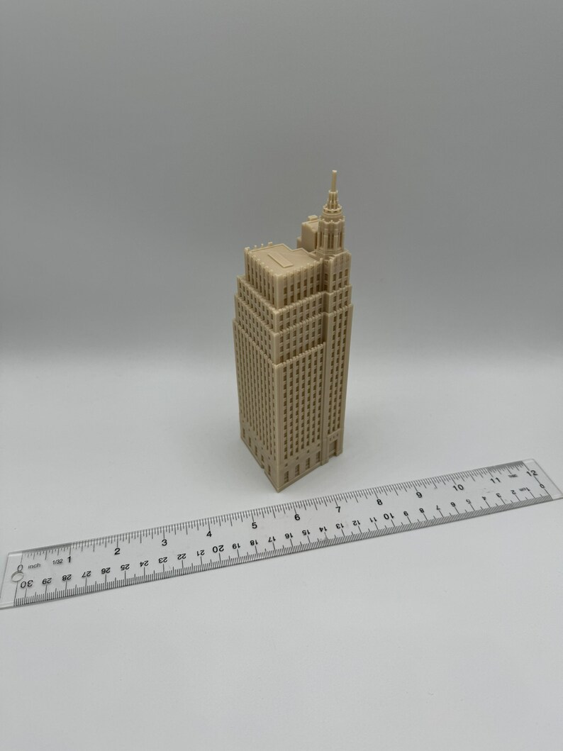 Pu&ograve; includere: Un modello in miniatura beige di un edificio alto con un tetto a punta e molte finestre. Il modello &egrave; alto circa 15 cm e si trova su una superficie bianca.
