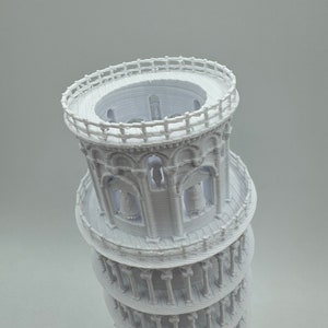 May include: A white 3D printed model of the Leaning Tower of Pisa. The model is detailed with arches, columns, and a railing at the top.