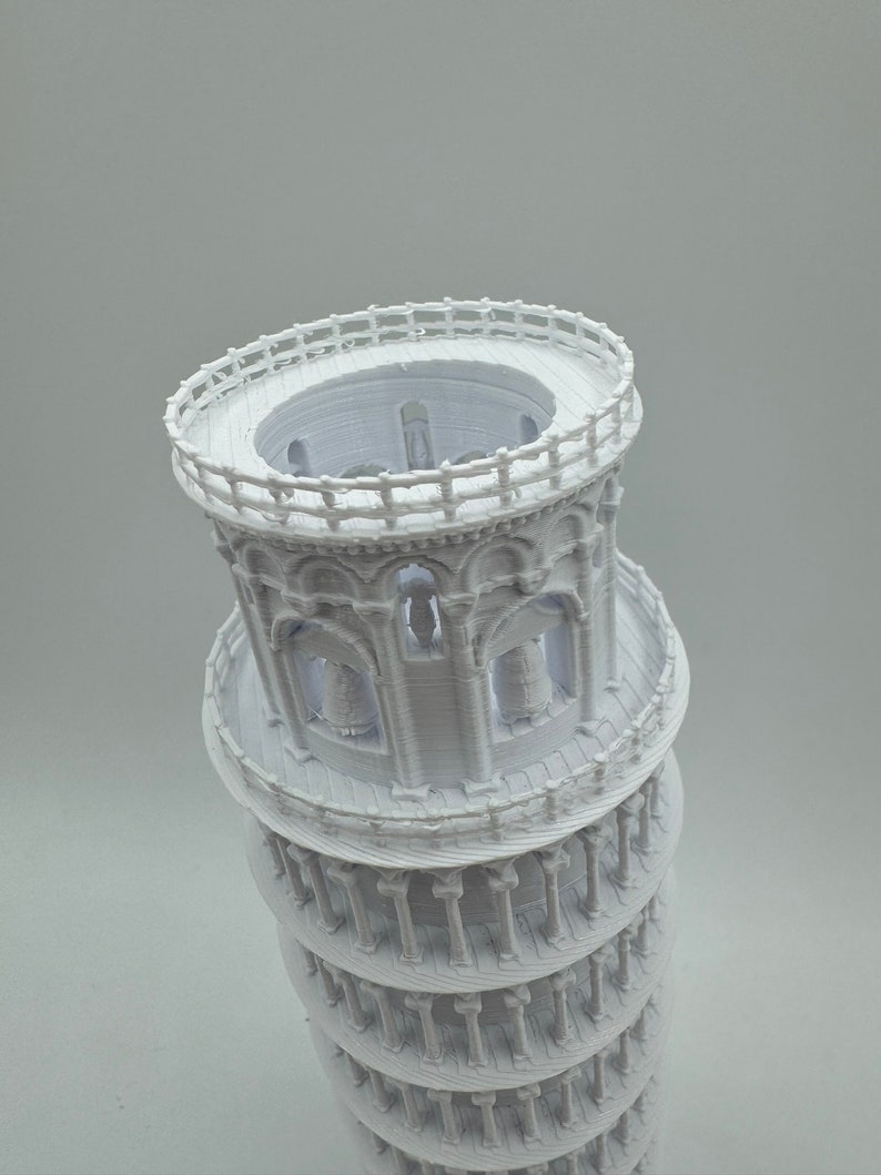 May include: A white 3D printed model of the Leaning Tower of Pisa. The model is detailed with arches, columns, and a railing at the top.