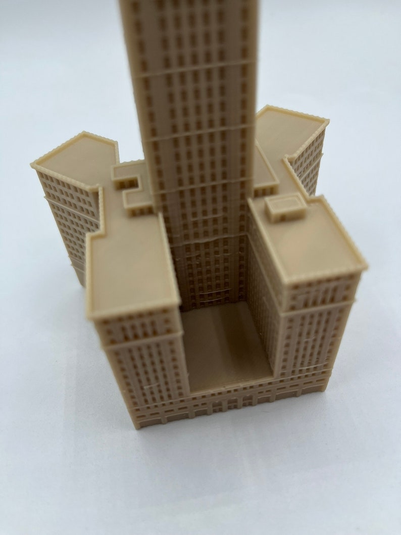 May include: A beige 3D printed model of a tall skyscraper building with a square base and a rectangular opening in the center.