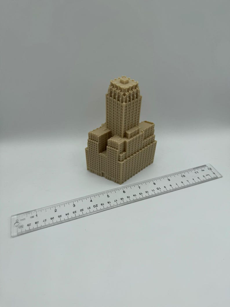 May include: A tan-colored miniature building model with a detailed architectural design. A clear ruler with inch measurements is placed next to the model. The model appears to be approximately 4 inches tall.