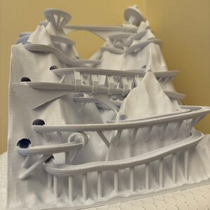Puede incluir: Un modelo 3D impreso en blanco de una estructura compleja con m&uacute;ltiples niveles, puentes y caminos sinuosos. El modelo parece ser un parque de atracciones en miniatura o un paisaje de fantas&iacute;a.