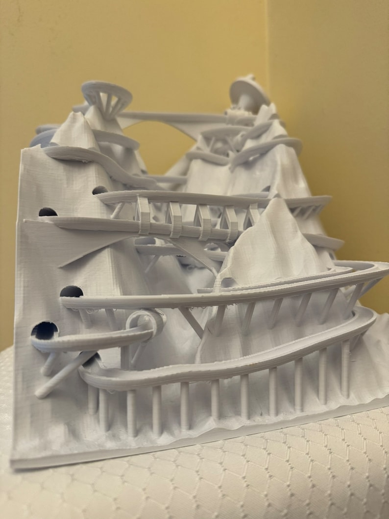 Puede incluir: Un modelo 3D impreso en blanco de una estructura compleja con m&uacute;ltiples niveles, puentes y caminos sinuosos. El modelo parece ser un parque de atracciones en miniatura o un paisaje de fantas&iacute;a.