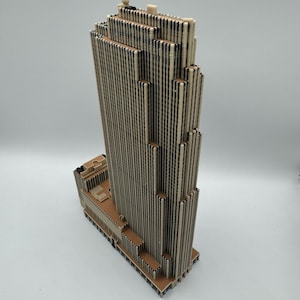 Puede incluir: Maqueta detallada de un rascacielos, construida con materiales beige y negros. El edificio presenta un dise&ntilde;o escalonado con l&iacute;neas verticales y una base plana. La parte superior del edificio tiene peque&ntilde;os elementos decorativos.
