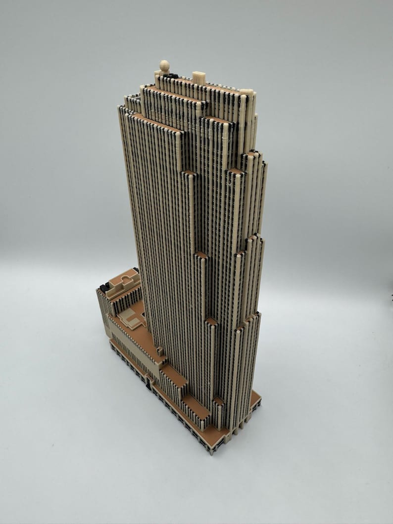 Puede incluir: Maqueta detallada de un rascacielos, construida con materiales beige y negros. El edificio presenta un dise&ntilde;o escalonado con l&iacute;neas verticales y una base plana. La parte superior del edificio tiene peque&ntilde;os elementos decorativos.