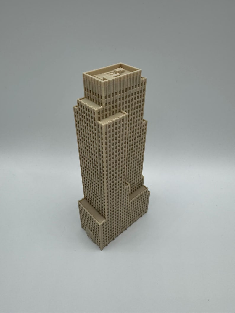May include: A beige, multi-story skyscraper model with a rectangular base and a stepped design. The building features numerous small, square windows and a flat roof. The model is set against a plain, light gray background.