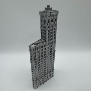 May include: A grey, 3D-printed model of a tall, ornate building. The building has a unique, flatiron shape with many windows and architectural details. The model is set against a plain, light grey background.