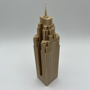 May include: A beige 3D printed model of a skyscraper with a pointed roof and many windows.