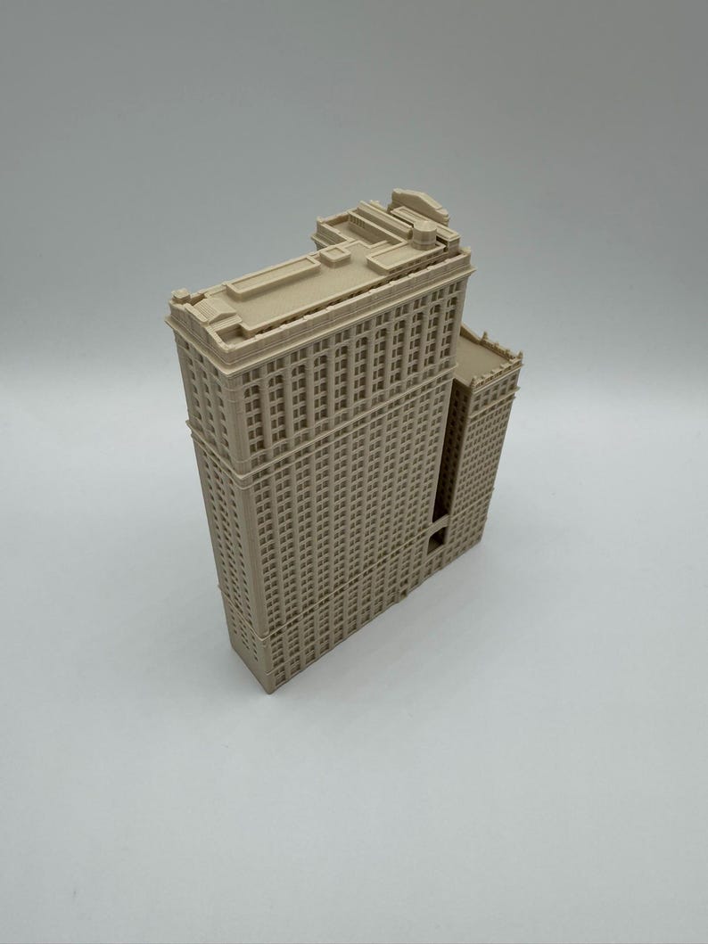 May include: A beige architectural model of a tall building with many windows. The building has a rectangular shape with a flat roof and detailed facade. The model is a miniature replica of a skyscraper.