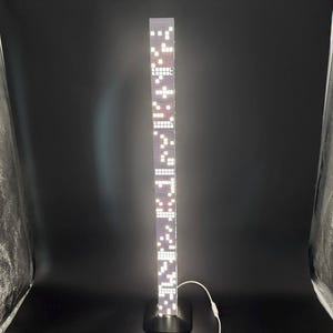 May include: A tall, rectangular LED floor lamp with a black base. The lamp's body is a series of illuminated white squares and rectangles. A white power cord extends from the base. The lamp is approximately 60 inches tall.