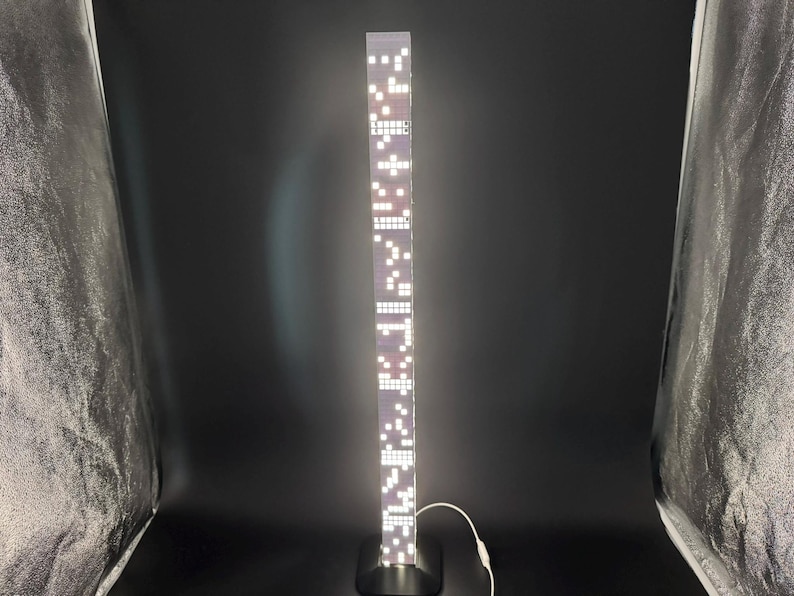 May include: A tall, rectangular LED floor lamp with a black base. The lamp's body is a series of illuminated white squares and rectangles. A white power cord extends from the base. The lamp is approximately 60 inches tall.