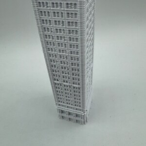 May include: A white 3D printed model of a tall building with many windows.