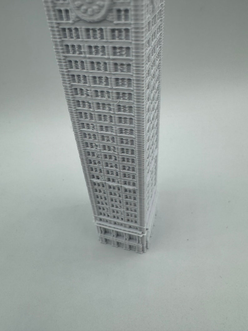 May include: A white 3D printed model of a tall building with many windows.