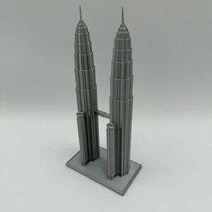 May include: A gray 3D printed model of the Petronas Towers in Kuala Lumpur, Malaysia. The model is detailed and includes the iconic skybridge connecting the two towers.