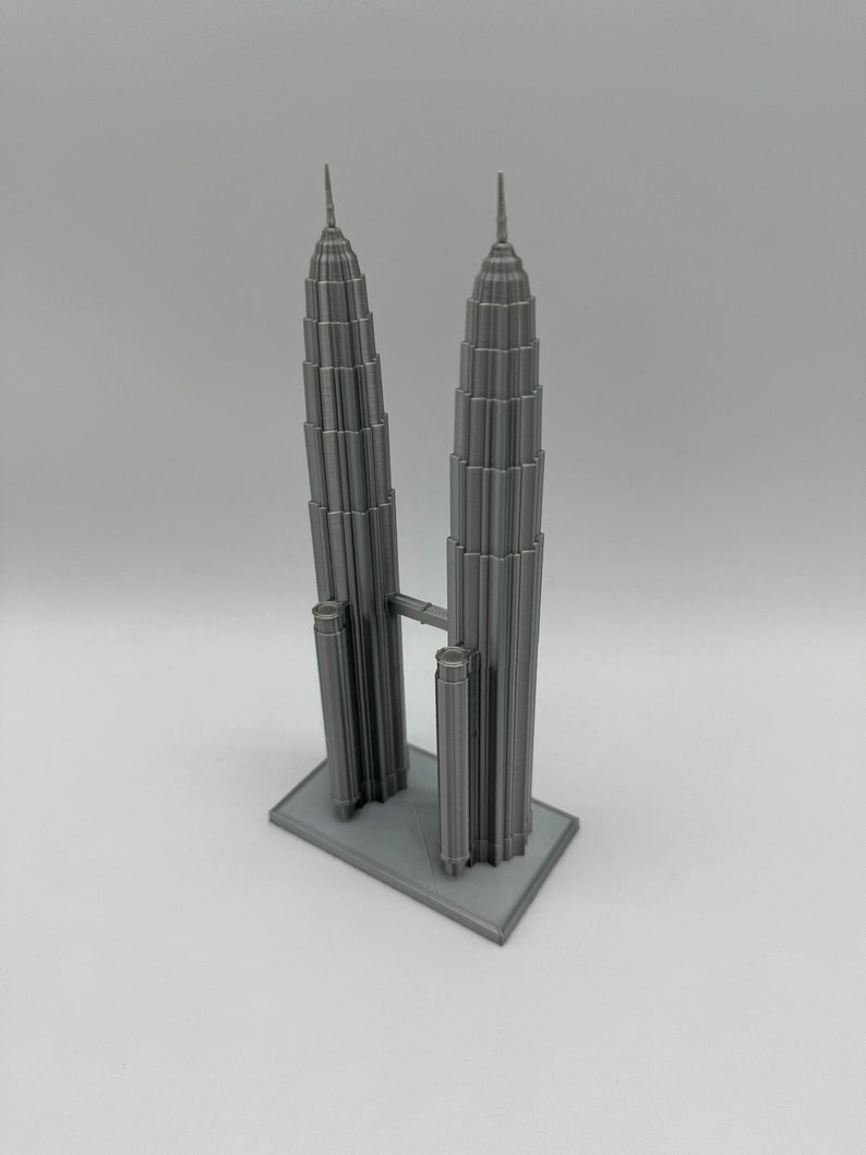May include: A gray 3D printed model of the Petronas Towers in Kuala Lumpur, Malaysia. The model is detailed and includes the iconic skybridge connecting the two towers.