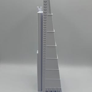 May include: A light gray architectural model of a tall skyscraper with a distinctive, angular design. The model features detailed structural elements, including a lattice-like framework at the top and a series of tiered sections. The building sits on a rectangular base.