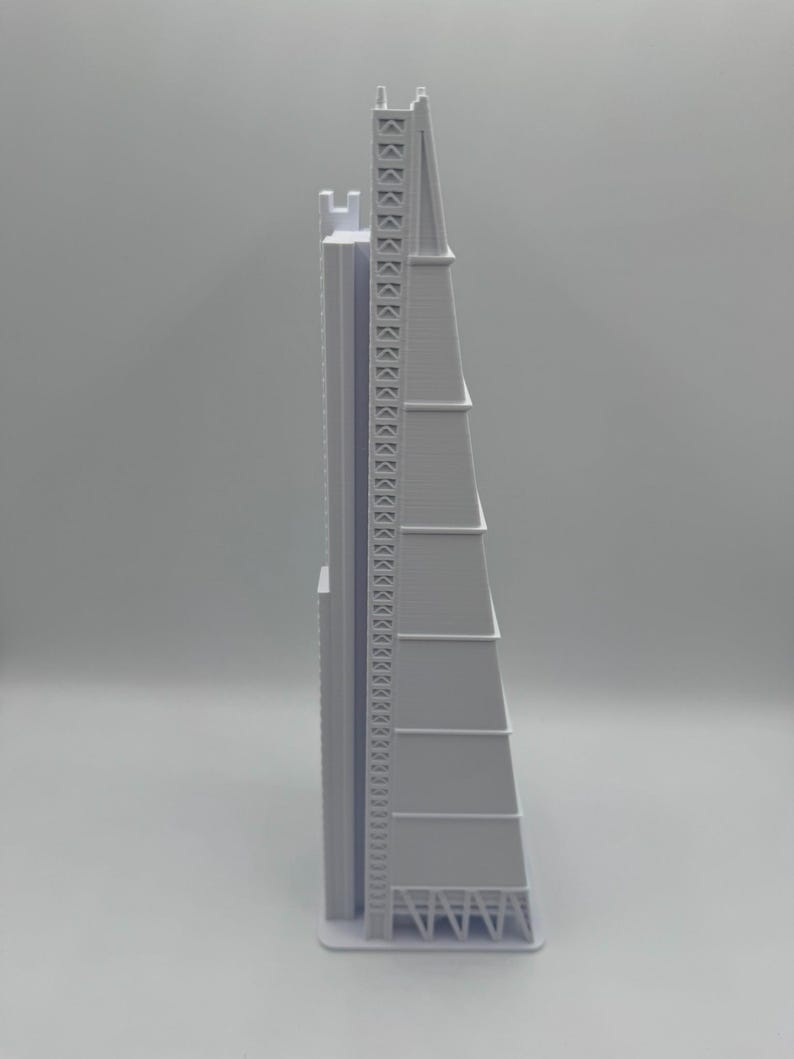 May include: A light gray architectural model of a tall skyscraper with a distinctive, angular design. The model features detailed structural elements, including a lattice-like framework at the top and a series of tiered sections. The building sits on a rectangular base.