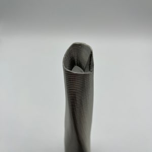 Op de afbeelding: Een grijze, gedraaide, 3D-geprinte vaas met een textuur.
