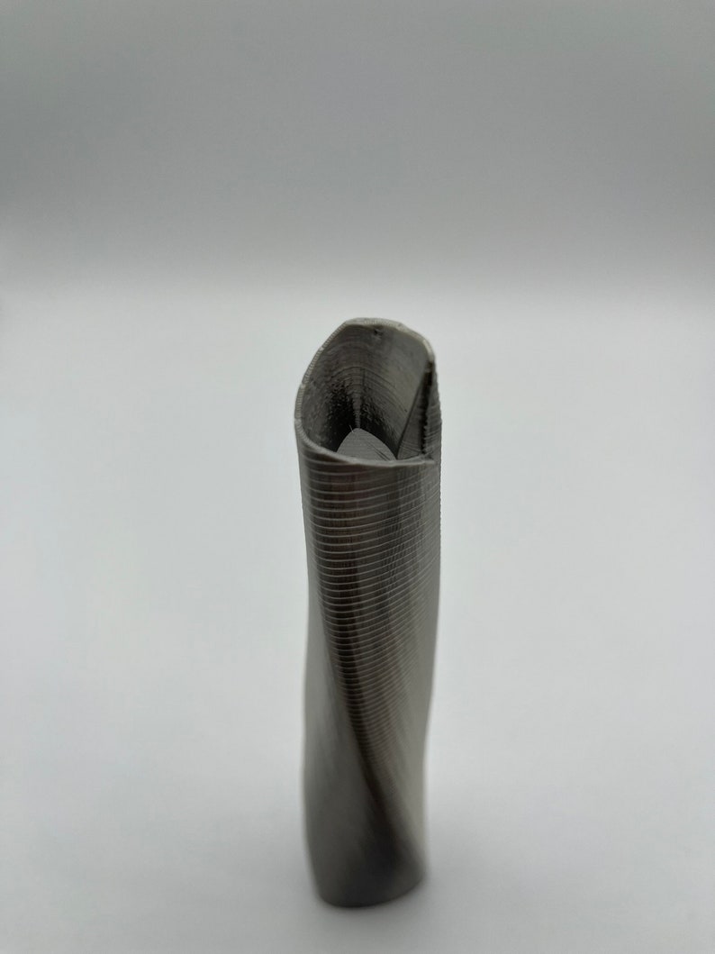 Op de afbeelding: Een grijze, gedraaide, 3D-geprinte vaas met een textuur.
