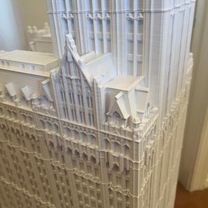 May include: A white 3D printed model of a tall building with intricate details and a pointed roof.