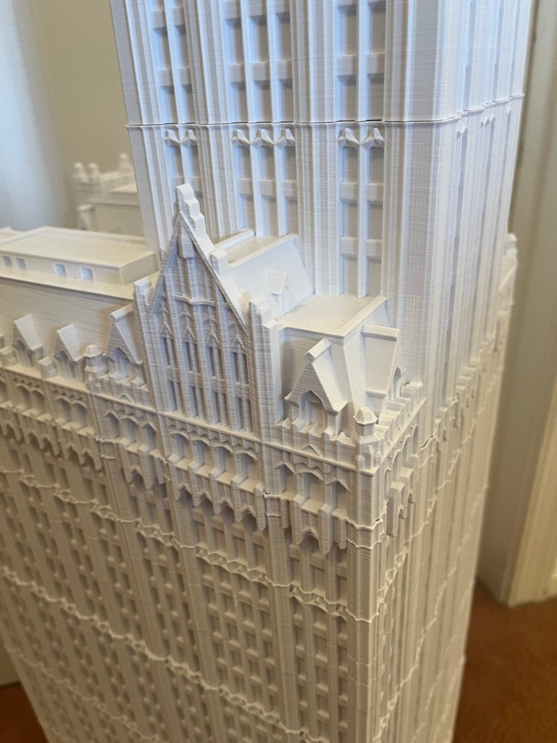 May include: A white 3D printed model of a tall building with intricate details and a pointed roof.