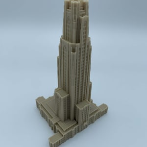 May include: A detailed 3D printed model of a tall, beige building with a pointed roof and many windows. The building has a rectangular base and is set against a plain white background.