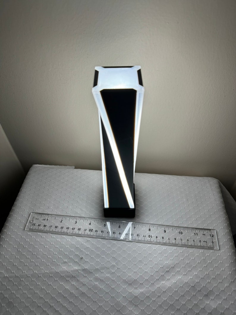 May include: A black and white geometric lamp with a white light source. The lamp is about 7 inches tall.