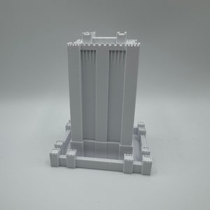 May include: A white 3D printed model of a tall tower with a square base and a crenellated top.