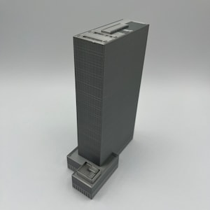 May include: A gray model of a tall skyscraper with a flat roof and a smaller building attached to the base.