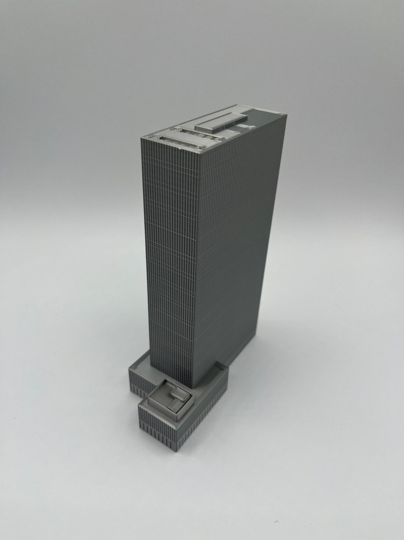 May include: A gray model of a tall skyscraper with a flat roof and a smaller building attached to the base.
