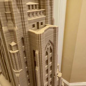 Puede incluir: Primer plano de una maqueta de un edificio alto impreso en 3D con detalles intrincados. El edificio est&aacute; hecho de pl&aacute;stico marr&oacute;n claro y tiene una superficie texturizada. La maqueta es una representaci&oacute;n de un edificio de estilo g&oacute;tico con arcos apuntados y elementos decorativos.