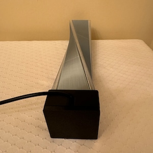 May include: A silver-colored, twisted, geometric lamp with a black base and a black cord.