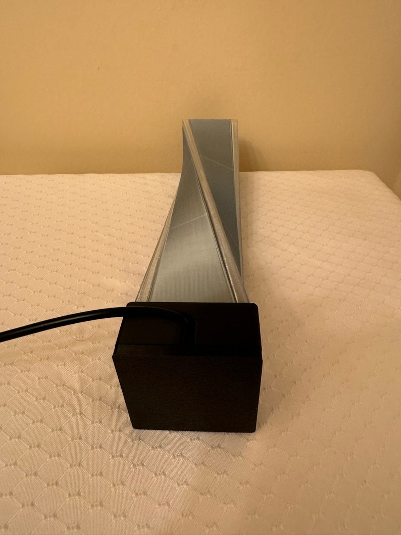 May include: A silver-colored, twisted, geometric lamp with a black base and a black cord.